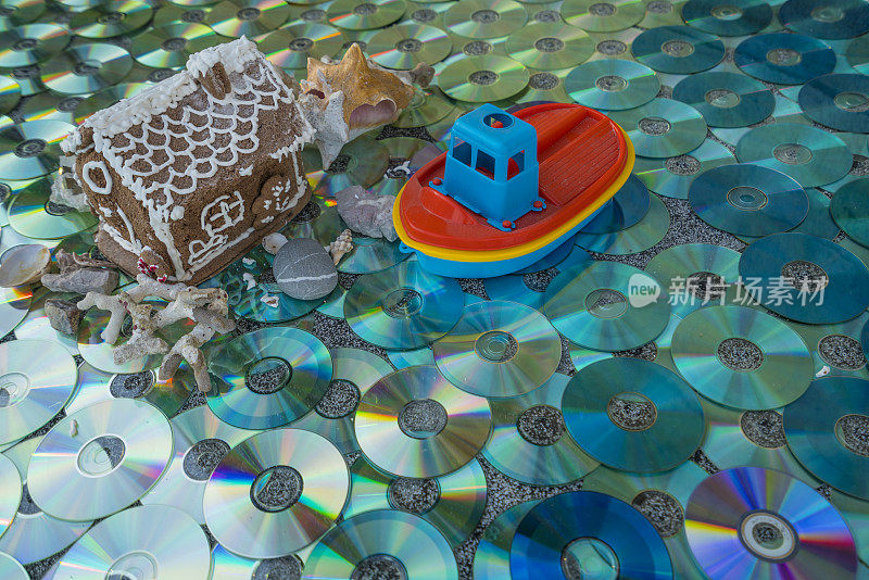 甜蜜的房子在岩石上与贝壳和船后的太阳反射，如在水中的彩色CD/DVD作为纹理背景